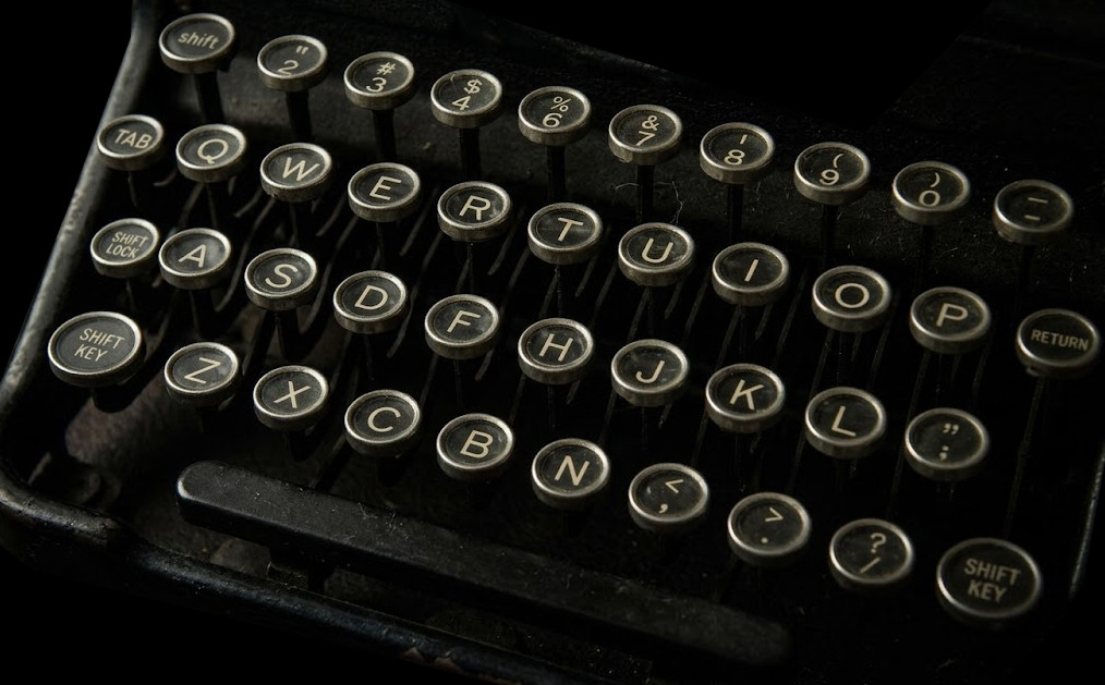 A close-up photograph of a vintage typewriter keys against a dark background.